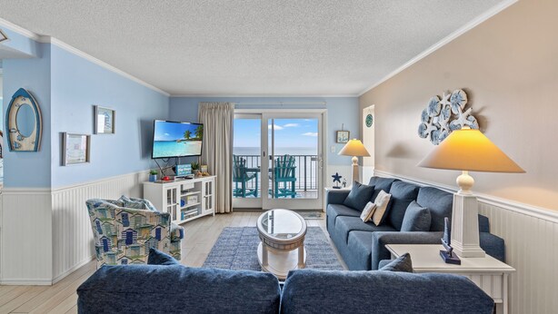 Een woonkamer met een bank, fauteuils, een salontafel, een televisie en een balkon met uitzicht.
