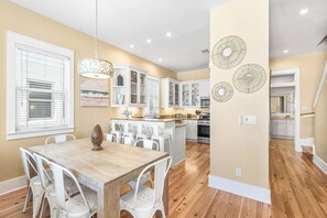 A modern kitchen with white cabinets, a wooden dining table, and a central island.