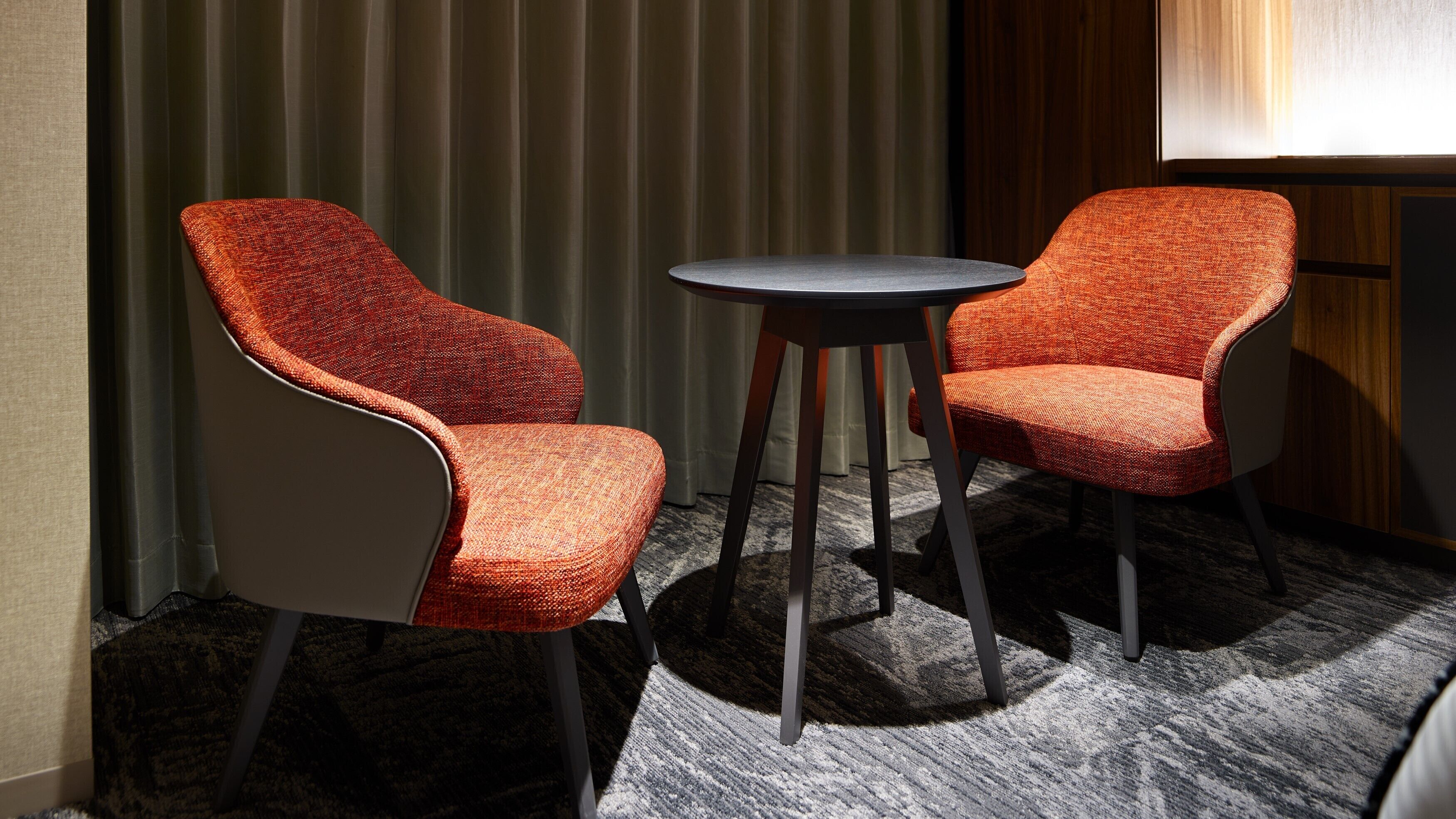 Two upholstered chairs with a woven texture, a small round table, and a carpeted floor.