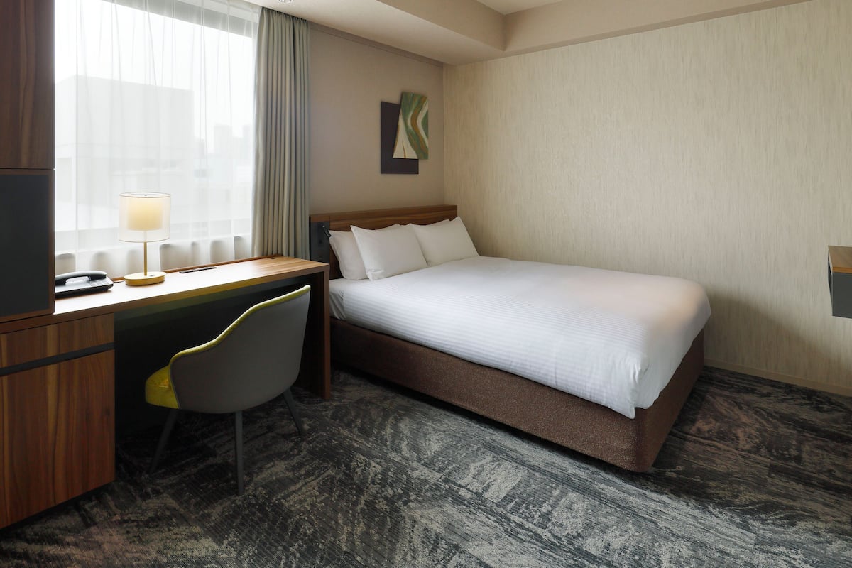 Ein Hotelzimmer mit Bett, Schreibtisch, Stuhl, Lampe und einem Bild an der Wand.