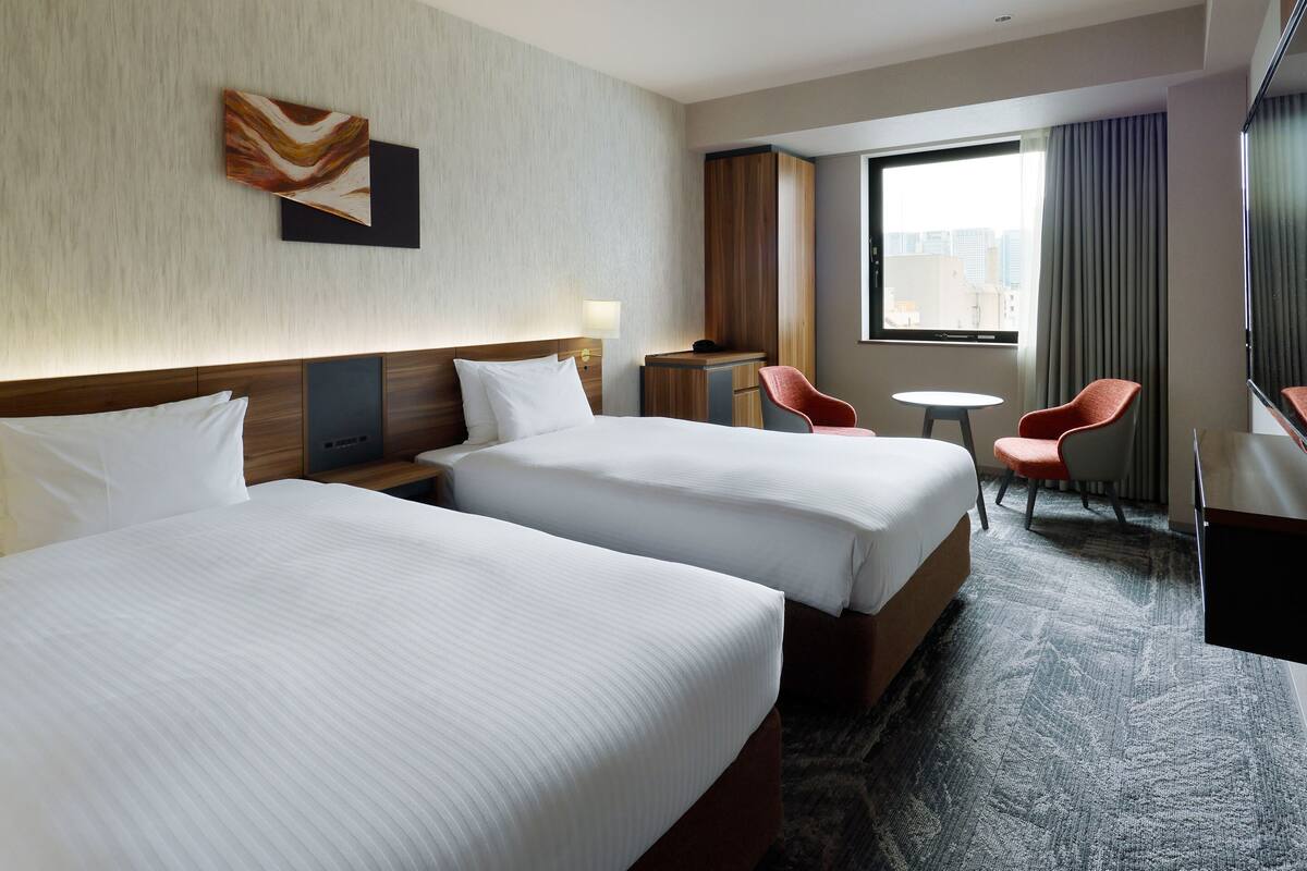 Ein Hotelzimmer mit zwei Betten, einem Schreibtisch, einem Stuhl und einem großen Fenster.