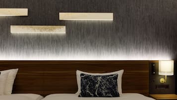 A hotel room with a wooden headboard, a marble-patterned pillow, a nightstand with a lamp, and wall-mounted light fixtures.
