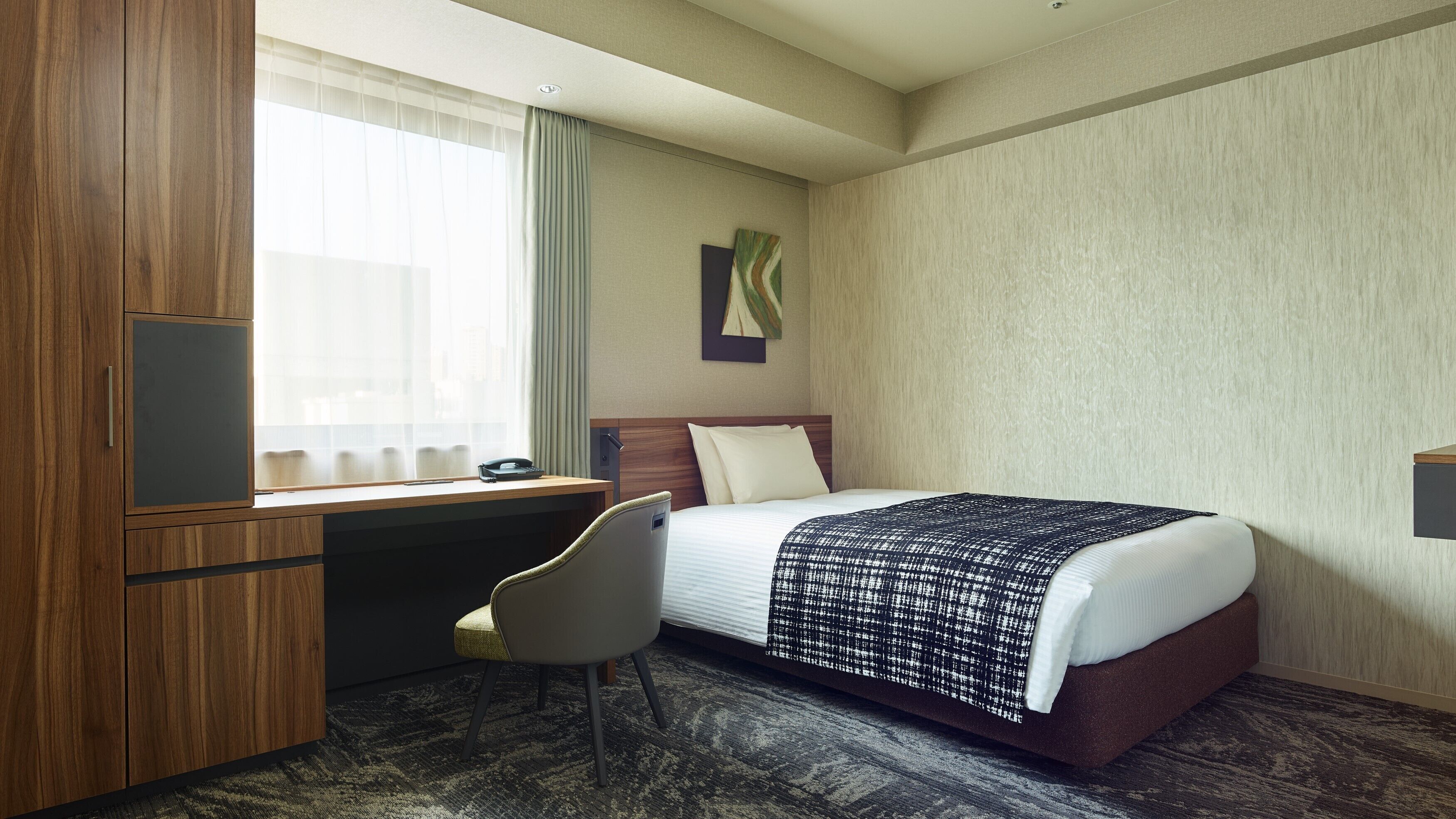 A hotel room with a bed, desk, chair, and a window with curtains.