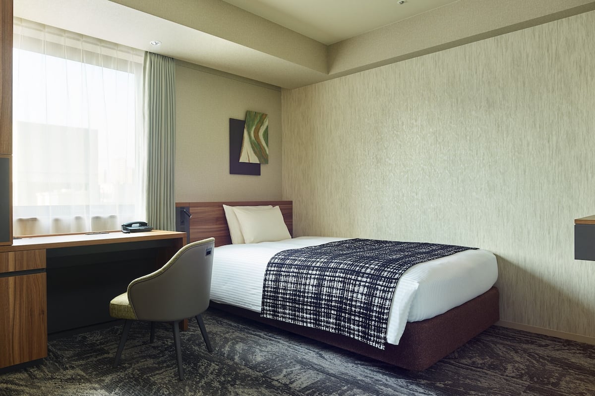 A hotel room with a bed, desk, chair, and a window with curtains.
