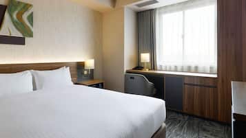 Ein Hotelzimmer mit einem großen Bett, einem Schreibtisch mit Lampe, einem Sessel und einem Fenster mit Vorhängen.