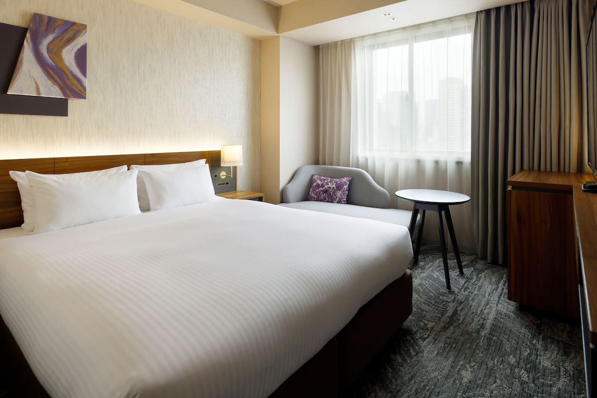 Ein Hotelzimmer mit einem großen Bett, einem Schreibtisch, einem Stuhl und einem Vorhangfenster.