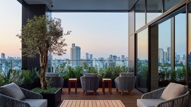 A modern balcony with wicker furniture, a wooden table, and a large tree. - Mitsui Garden Hotel Gotanda Tokyo (Tokyo)