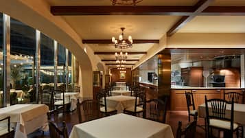 A restaurant interior with tables, chairs, a bar area, and a view through large windows.