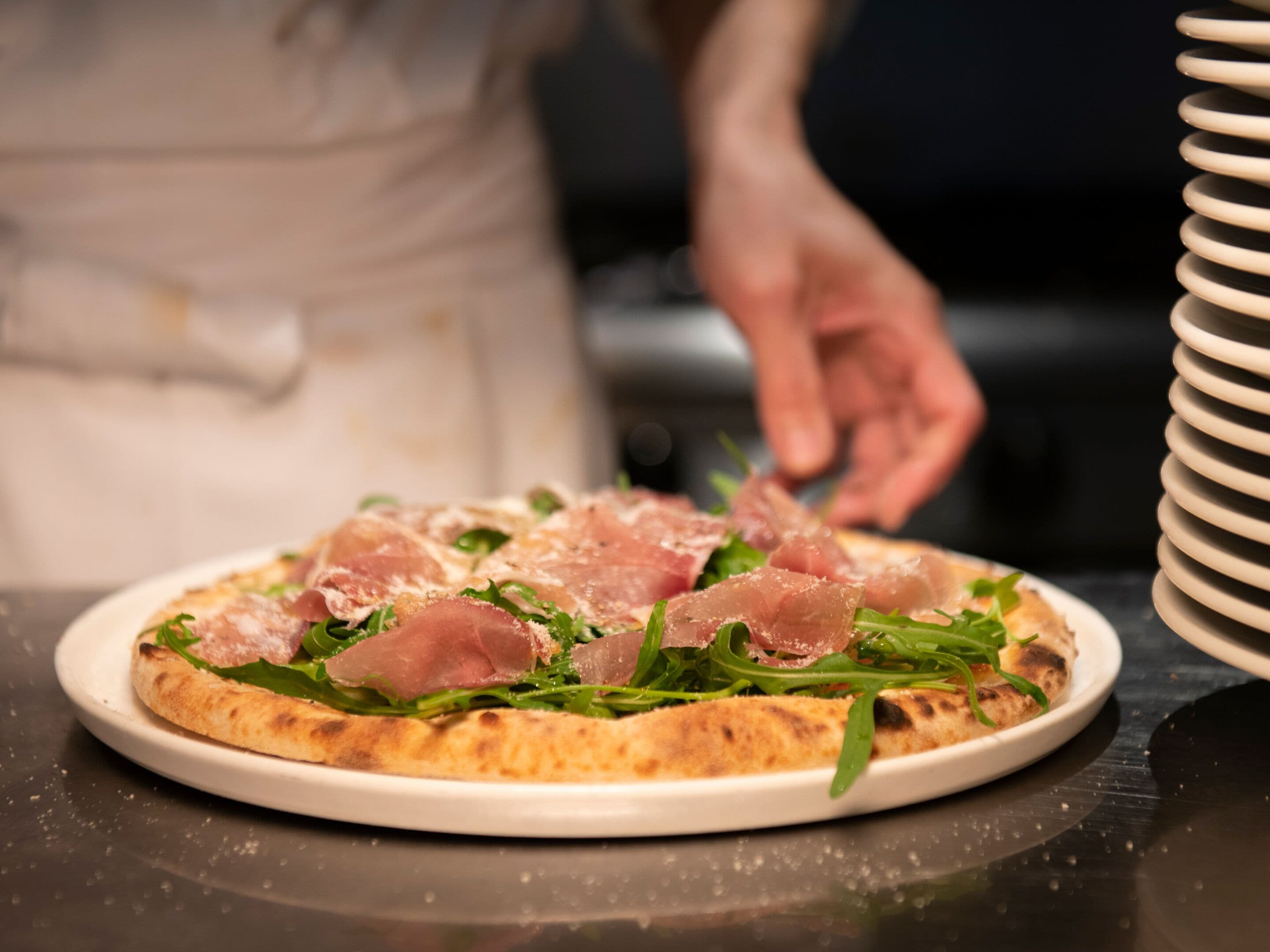 Pizza con jamón de Parma y hojas verdes sobre un plato blanco.