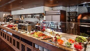 Buffet com diversos alimentos e área de cozinha ao fundo.