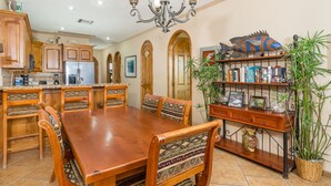 Uma sala de jantar com mesa e cadeiras de madeira, um candelabro e uma estante de livros e objetos decorativos.