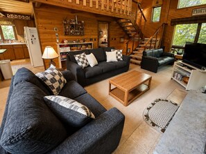 A cozy cabin interior with a living area featuring sofas, a coffee table, a TV, and a staircase leading to an upper level.