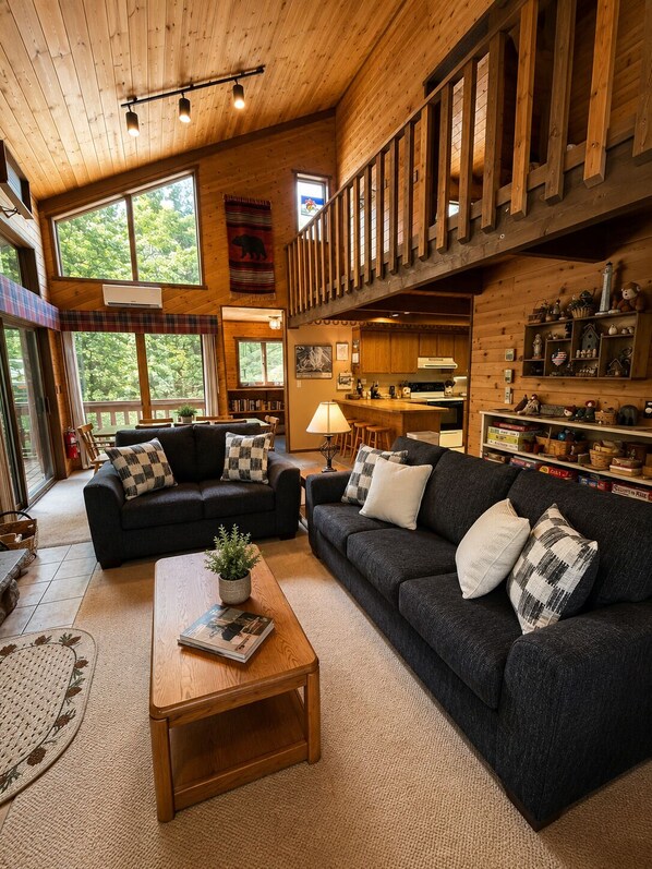 A spacious living room with a high ceiling, large windows, and a cozy fireplace.