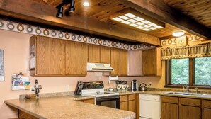 A kitchen with wooden cabinets, a granite countertop, a stove, a sink, and a window with a view of trees. - A Trailside Home with Indoor Hot Tub And Allows Dogs (Ironwood)
