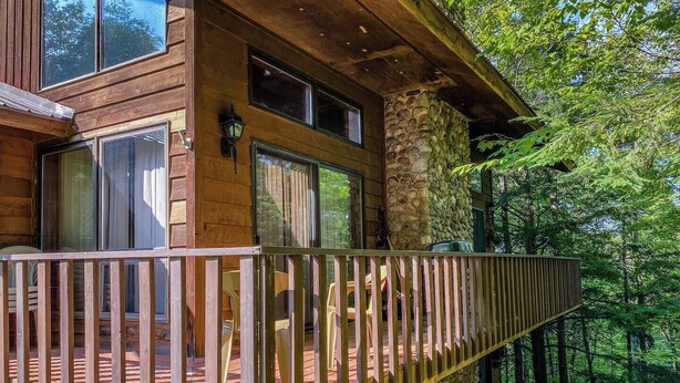A wooden cabin with a stone foundation, large windows, and a wooden deck. - A Trailside Home with Indoor Hot Tub And Allows Dogs (Ironwood)