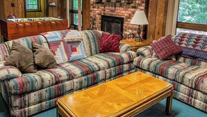 A cozy living room with a brick fireplace, a sofa set, and a foosball table. - A Trailside Home with Indoor Hot Tub And Allows Dogs (Ironwood)