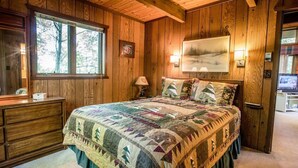 A wooden-paneled bedroom with a large bed, a dresser, a window, and a painting on the wall. - A Trailside Home with Indoor Hot Tub And Allows Dogs (Ironwood)