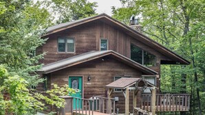 A two-story wooden cabin with a green door, a small porch, and a chimney. - A Trailside Home with Indoor Hot Tub And Allows Dogs (Ironwood)