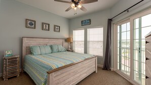 Quarto com cama de madeira, roupa de cama listrada, ventoinha no teto e uma janela grande com persianas.