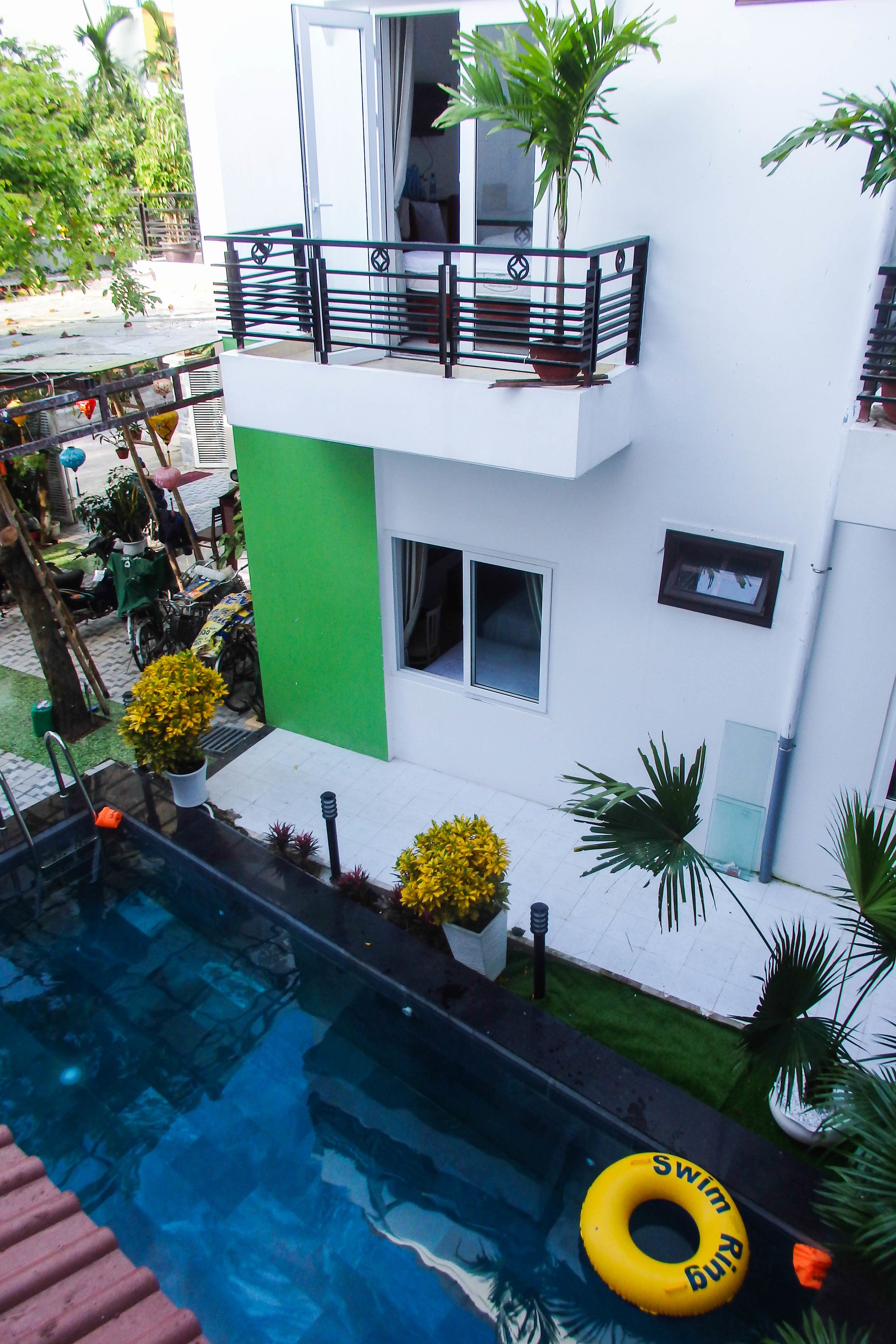 A modern two-story building with a swimming pool, surrounded by potted plants and a green wall.
