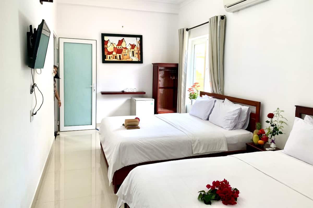 Habitación de hotel con dos camas, un televisor montado en la pared, un cuadro, un armario y un equipo de aire acondicionado.