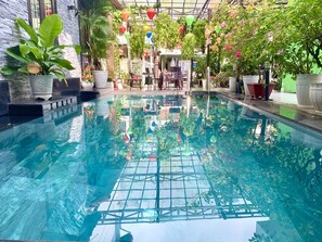 An indoor swimming pool with clear water, surrounded by potted plants and hanging decorations. - Ngoc Sinh Homestay (Da Nang)