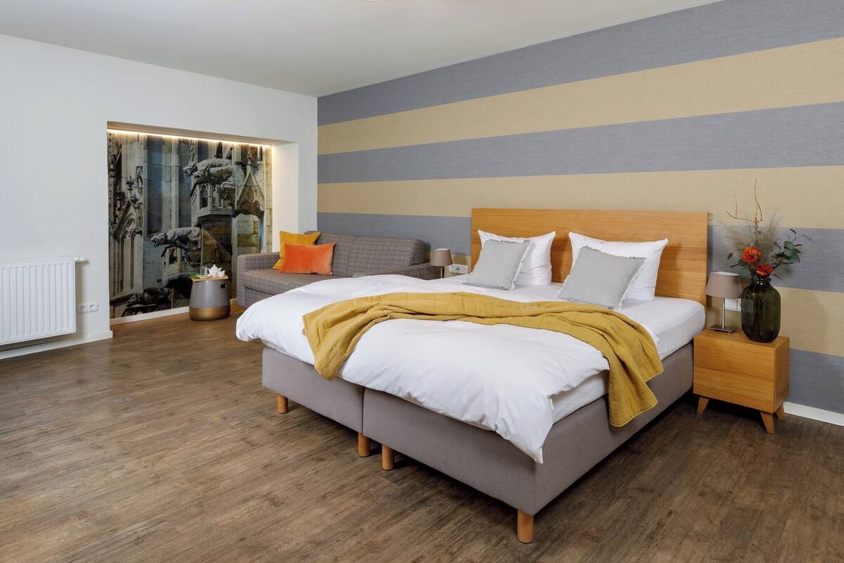 A modern bedroom with a large bed, a nightstand, a sofa, and a decorative wall.