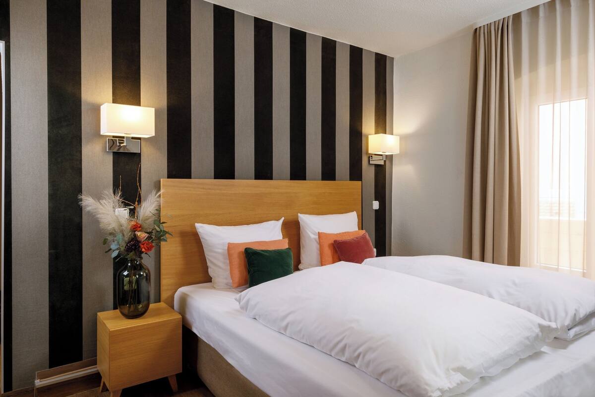 A hotel room with a large bed, two bedside tables, a vase with flowers, and a striped wall.