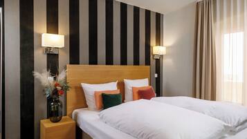 Habitación de hotel con una cama grande, dos mesitas de noche, un florero con flores y una pared a rayas.