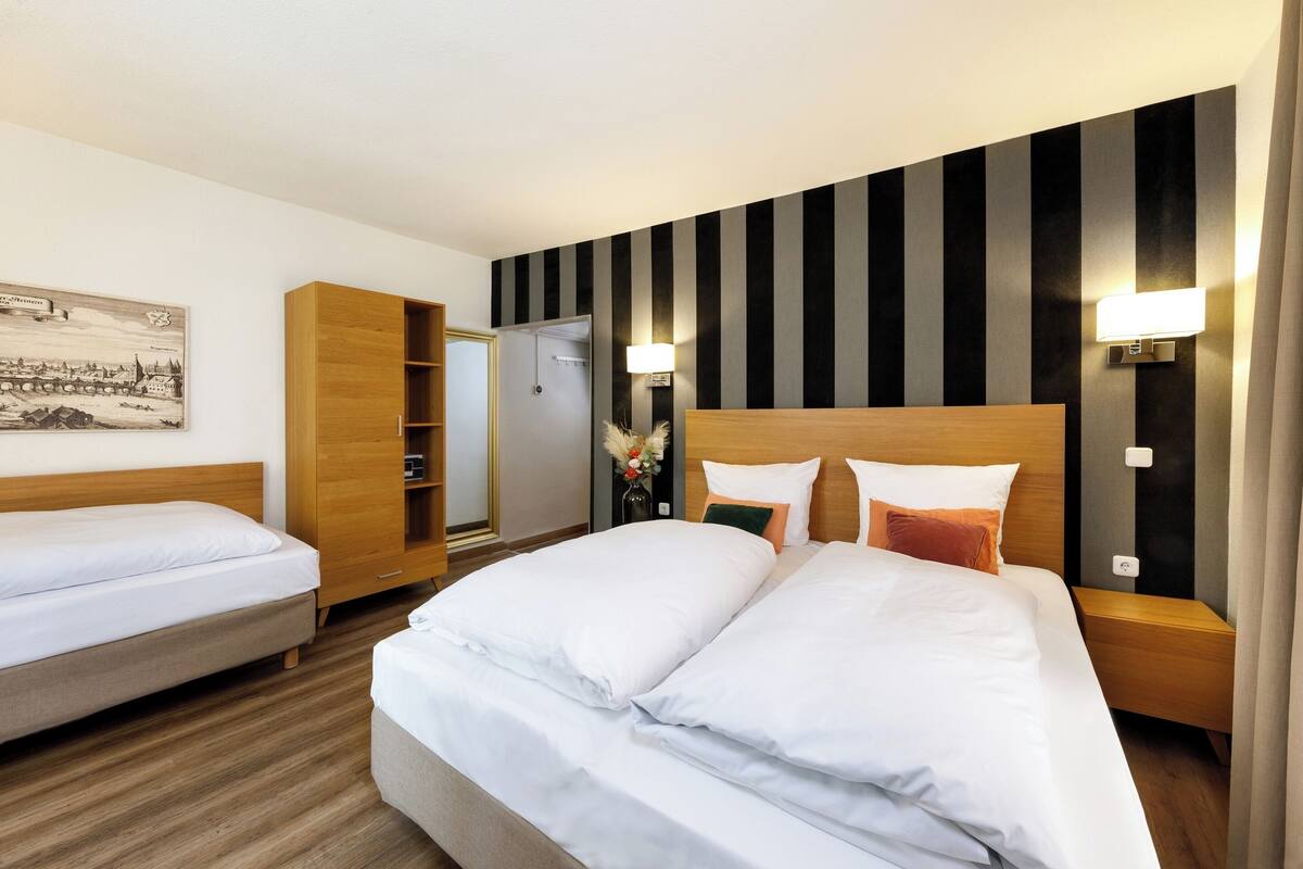 A hotel room with two beds, a wardrobe, a mirror, and a wall-mounted light fixture.