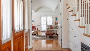 A spacious living room with a large window, a fireplace, and a staircase with wooden railings. - Gingerbread - Pacific Grove House - Close to Beach (Pacific Grove)