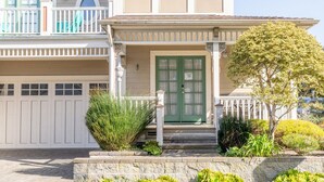 A two-story house with a green front door, a balcony with white railings, and a small garden with various plants. - Gingerbread - Pacific Grove House - Close to Beach (Pacific Grove)