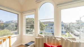 A room with a large window, a sofa with striped cushions, and a view of a residential area. - Gingerbread - Pacific Grove House - Close to Beach (Pacific Grove)