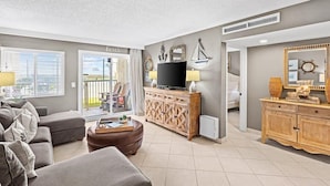 Uma sala de estar com sofá, televisão em um móvel de madeira e varanda com vista.