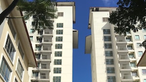A high-rise residential building with multiple balconies, a central entrance with a red awning, and surrounding greenery.