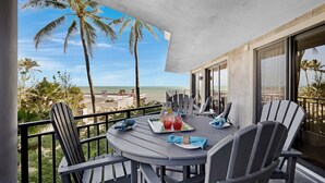 A balcony with a table set for two, overlooking a beach with palm trees and the ocean.