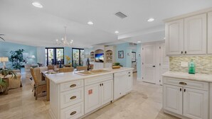 A spacious kitchen with white cabinetry, a large island, and a dining area with wicker furniture.