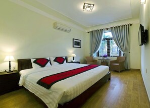 Una habitación de hotel con una cama grande, dos mesitas de noche, un escritorio con silla, una ventana con cortinas y un televisor montado en la pared.
