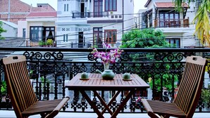 A balcony with a wooden table and two wooden chairs, a vase with flowers, and a view of buildings in the background. - An Hoi Town Homestay (Da Nang)