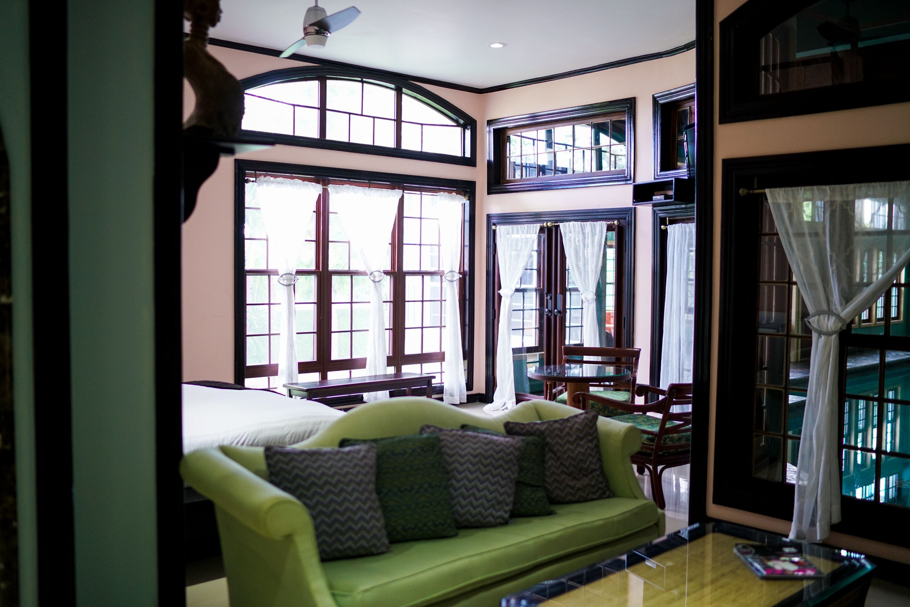 A room with a green sofa, a dining table with chairs, and large windows with curtains.