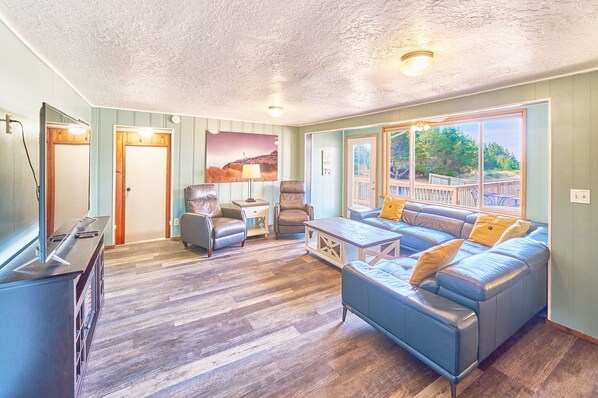 A spacious living room with a large sofa, two armchairs, a coffee table, and a television.