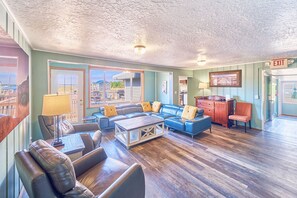 A spacious living room with a large sectional sofa, a coffee table, and a fireplace. There is a wooden cabinet and a chair in the corner.