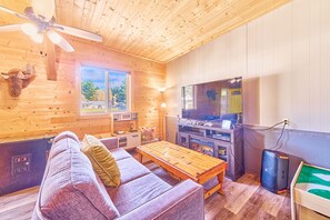 A cozy cabin interior with a wooden ceiling, a sofa, a coffee table, a TV, and a fireplace.