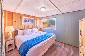 A bedroom with a bed, nightstands, a window, and wooden paneling.