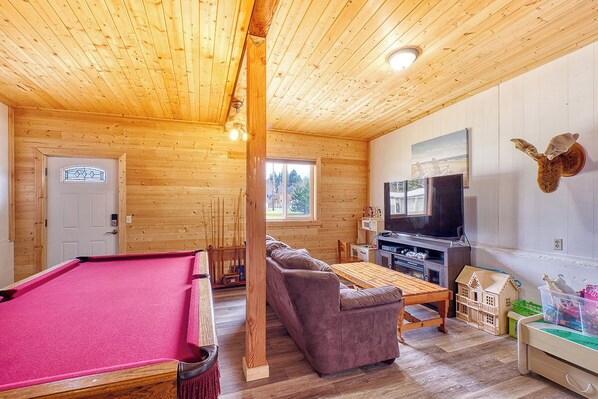 A wooden interior with a pool table, sofa, television, and children's play area.