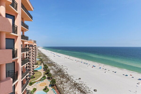 A beachfront hotel with multiple balconies, a pool, and a beach with umbrellas.