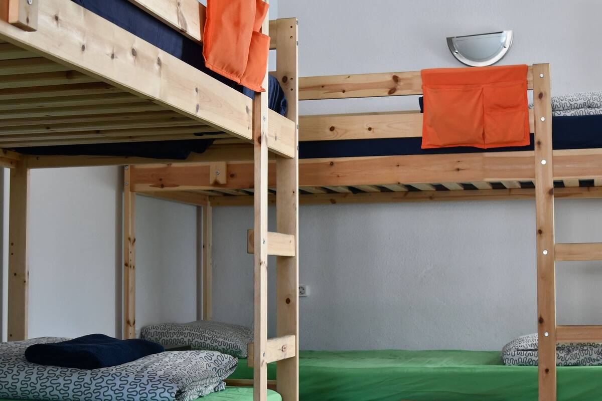 A bunk bed room with a green mattress, patterned pillows, and orange blankets.