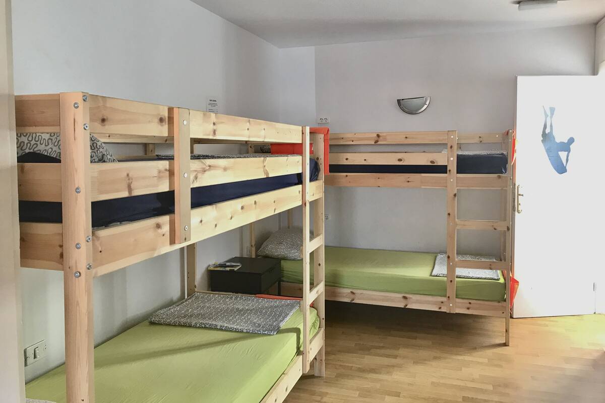 A room with three bunk beds, a small table, and a mirror on the wall.