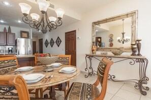 A dining area with a round glass table, patterned chairs, a decorative mirror, and a chandelier.