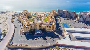 Un resort con varias edificaciones, un área de piscina central y una playa al fondo.